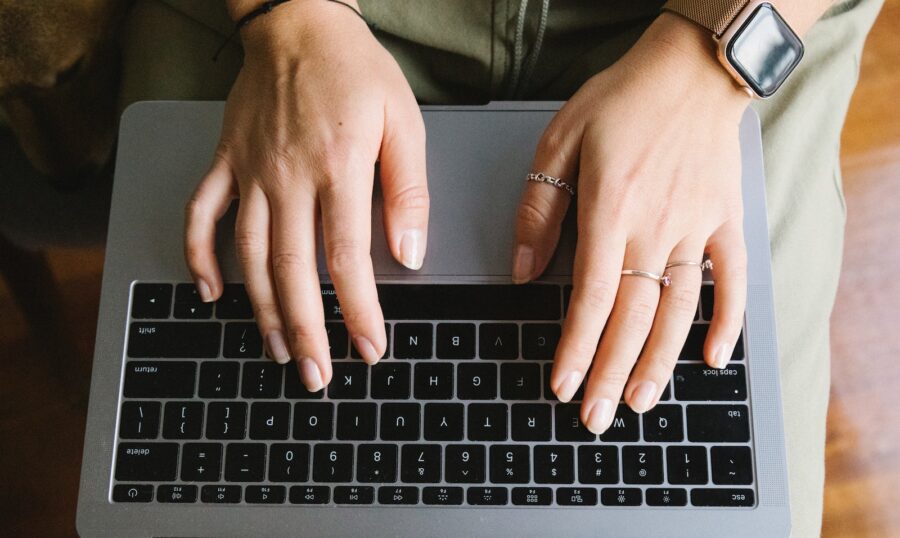 Top view crop anonymous female browsing modern netbook and typing on keyboard in light room