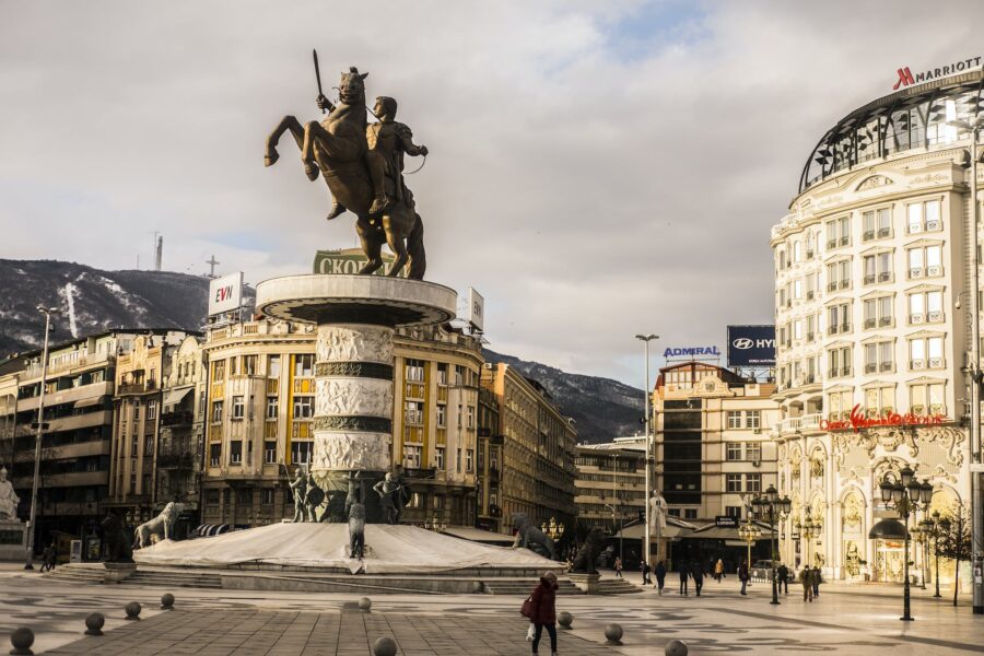 Aged stone sculpture of warrior on horse near house facades and snowy mountain under cloudy sky in town