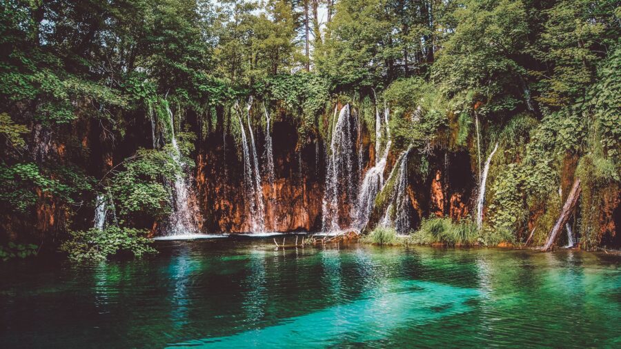 Amazing waterfall flowing through rocky cliff with green trees on sunny day