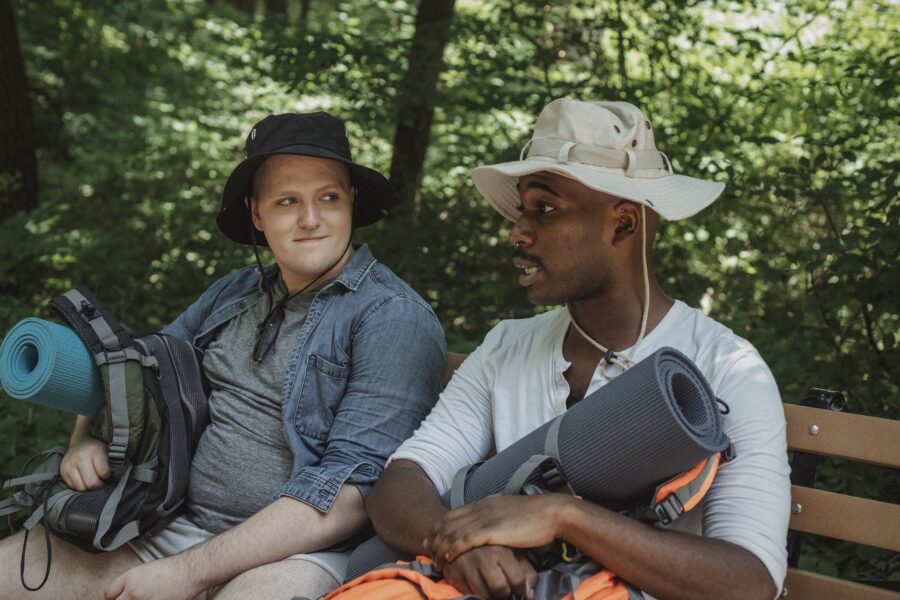 Multiethnic backpackers speaking on bench in woods