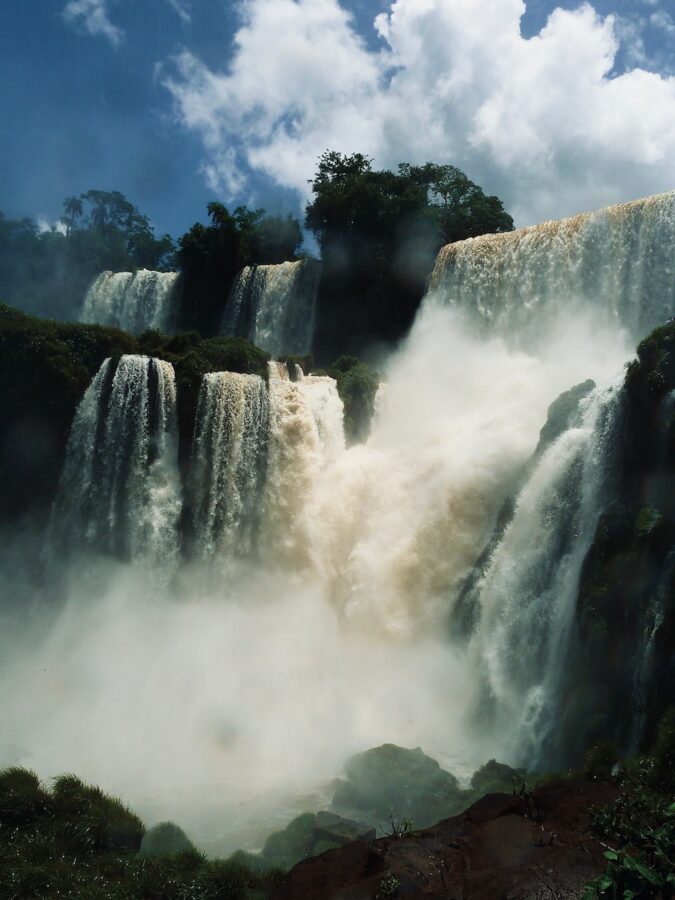 a large waterfall with trees and blue sky