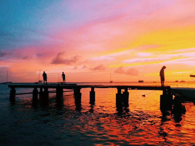 three people on boardwalk at the sea during sunset